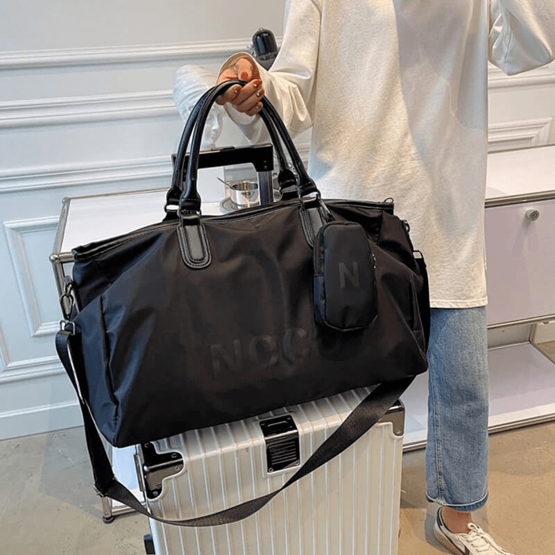 Unisex waterproof large shoulder bag in black nylon, perfect for fitness and travel. Stylish sports handbag on suitcase in modern setting.